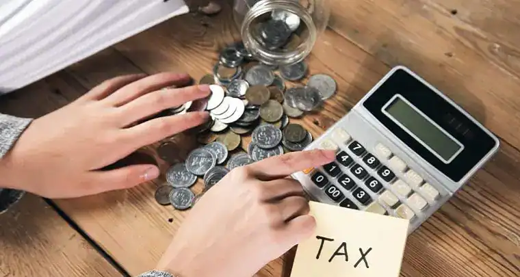 Coins and calculator on wooden table representing financial or tax calculations at ICT.
