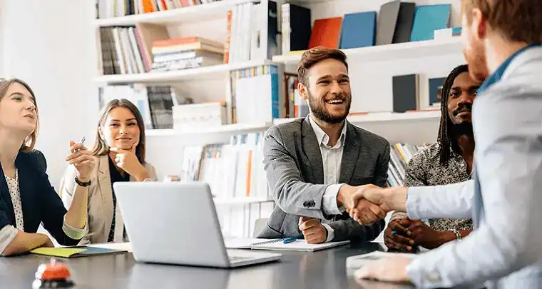 Handshake between diverse professionals in a modern library or office setting, representing ICT solutions, digital innovation, and technology-driven business collaboration.